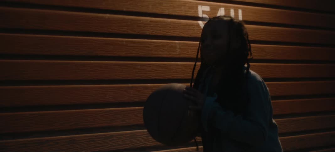 A girl dribbles a basketball under a light on the outside of a building at night