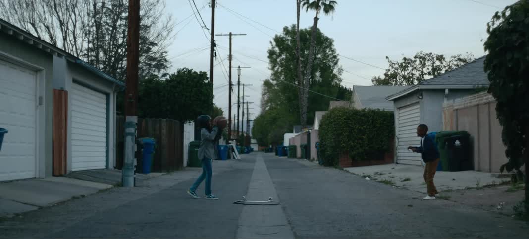 Boy and girl wearing helmet pass basketball back and forth standing in street between houses