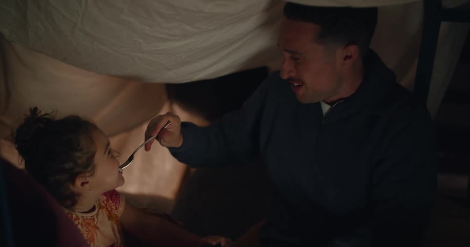A man feeds his daughter under the tent