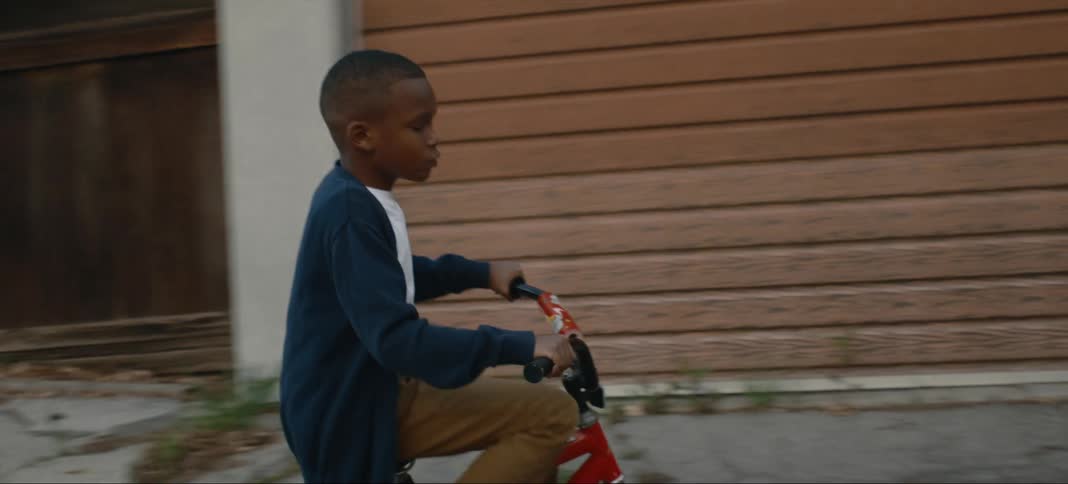 A young boy is riding a bicycle in his neighborhood near a fence and garbage cans