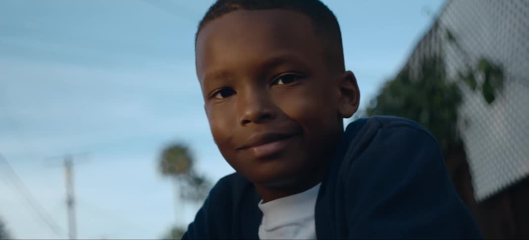 A boy poses while sitting outside near a fence
