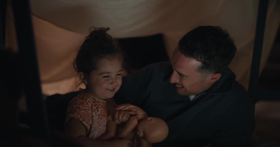 A dad and his little girl playing in a sheet fort and watching a video on a laptop