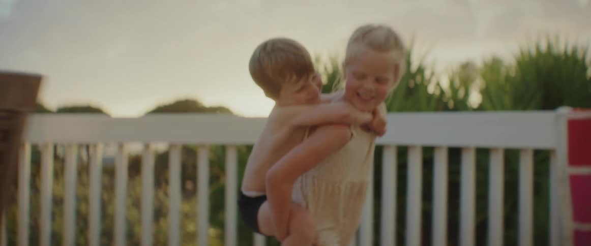 A girl gives her brother a piggyback ride across their patio