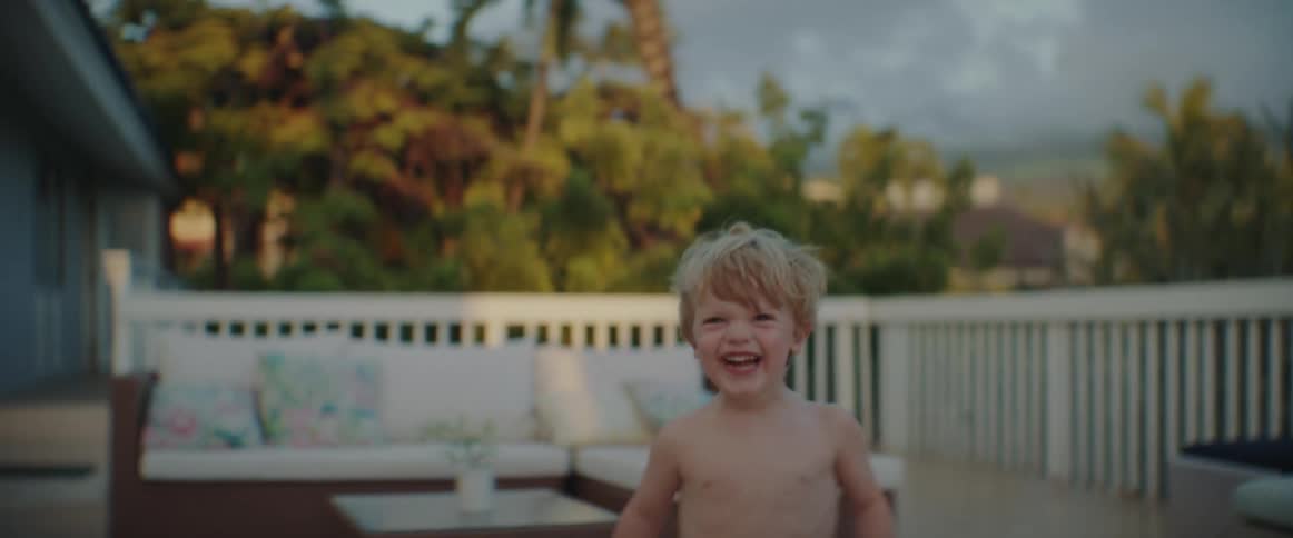 A little boy carrying a stuffed animal smiles and laughs as he runs around the patio