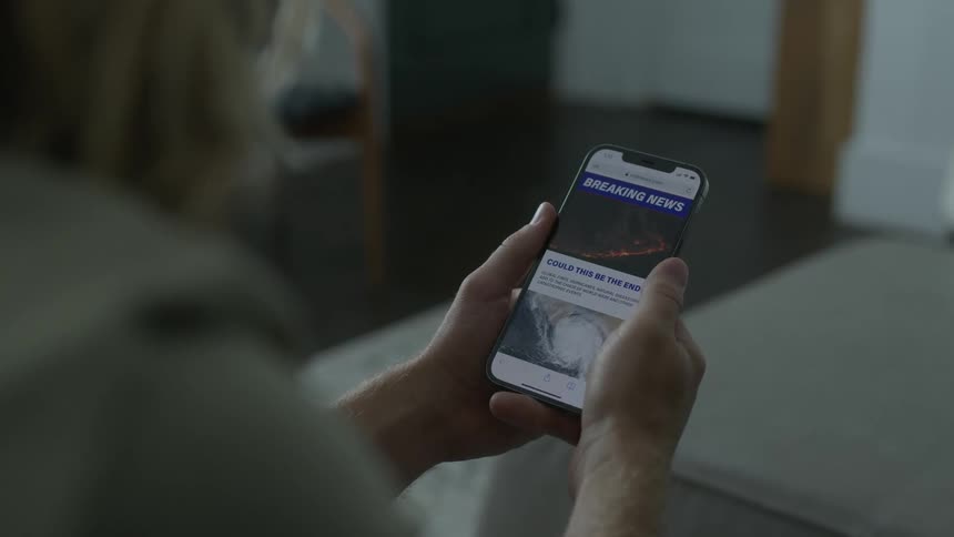 Man wearing hoodie reads news on smartphone and talks to another