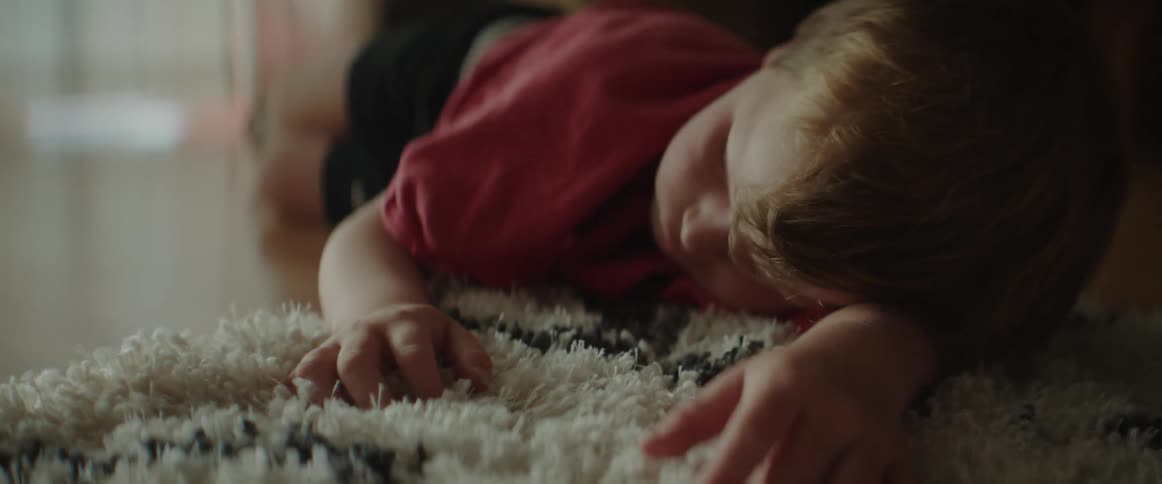 A young boy is lying on a floor with his head on a rug