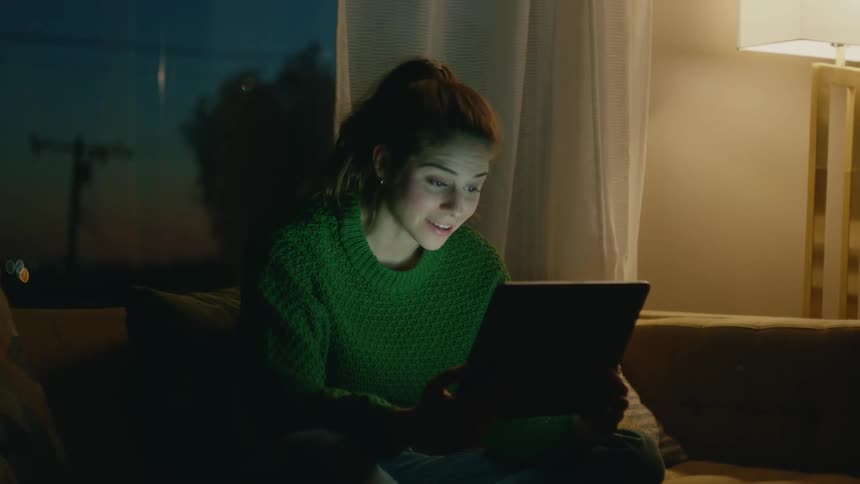 A woman sits at home in the evening and video chats on a tablet