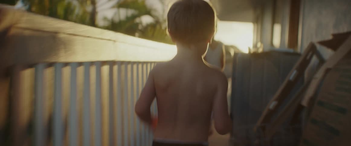 Boy chases his sister across balcony passing cardboard boxes on a sunny day