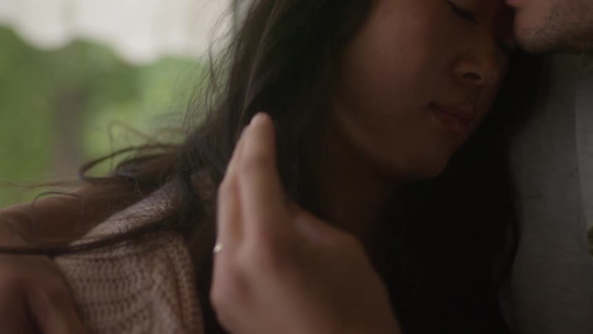 A woman rests her head on a mans shoulder and he kisses her as he caresses her face and hair