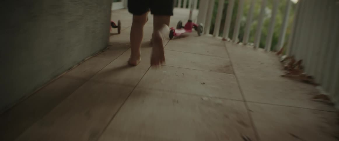 A little boy wearing shorts is running on a balcony outside chasing another child