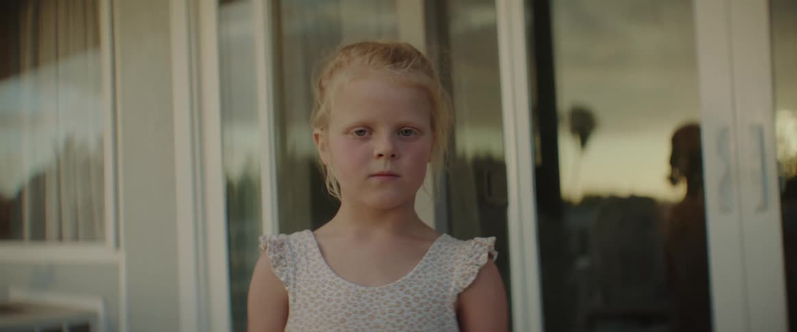 A young girl stands in front of sliding glass doors at home