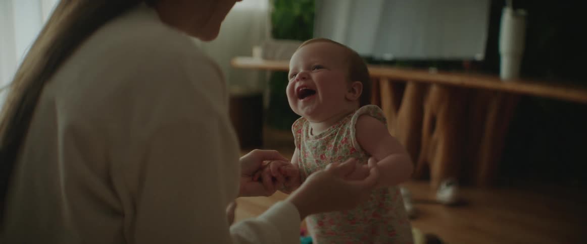 Mother holds on to baby girls hands helping the laughing child stand
