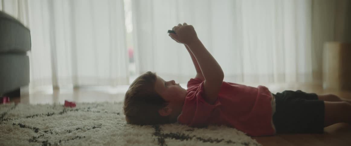 A child is laying indoors and playing video games