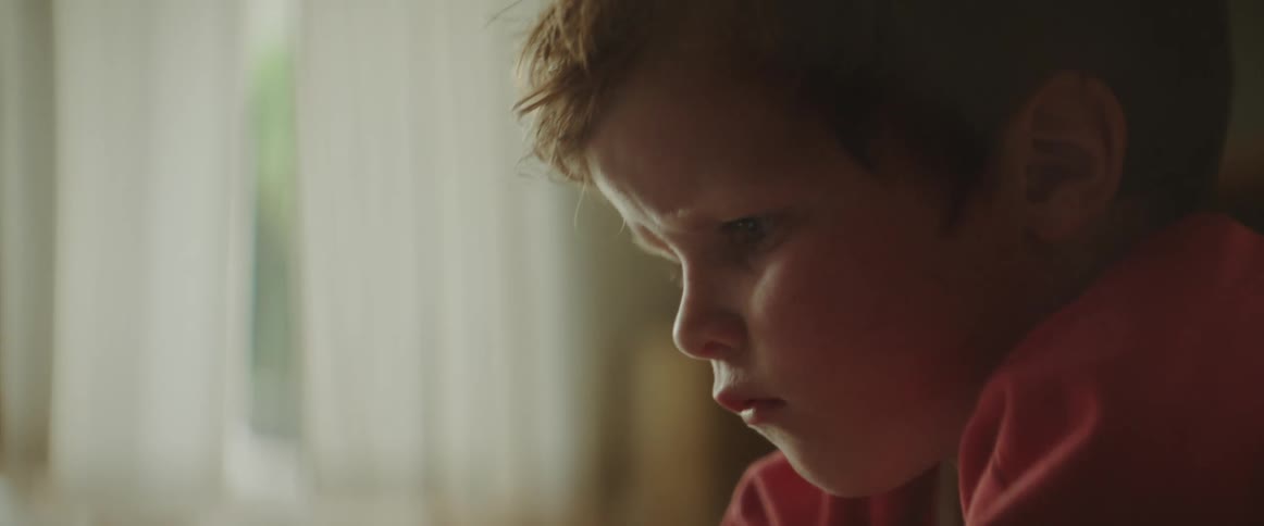 A young boy at home watches a screen on a cell phone