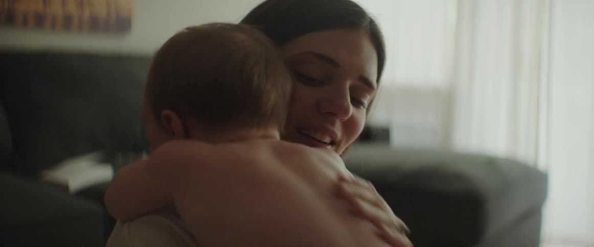 A woman is sitting on her living room floor and she picks up her baby and gives them a hug