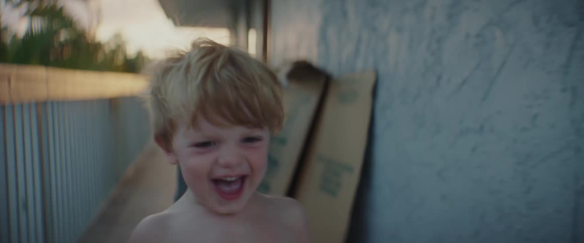 A little boy wearing shorts is laughing and smiling as he runs on a balcony outside