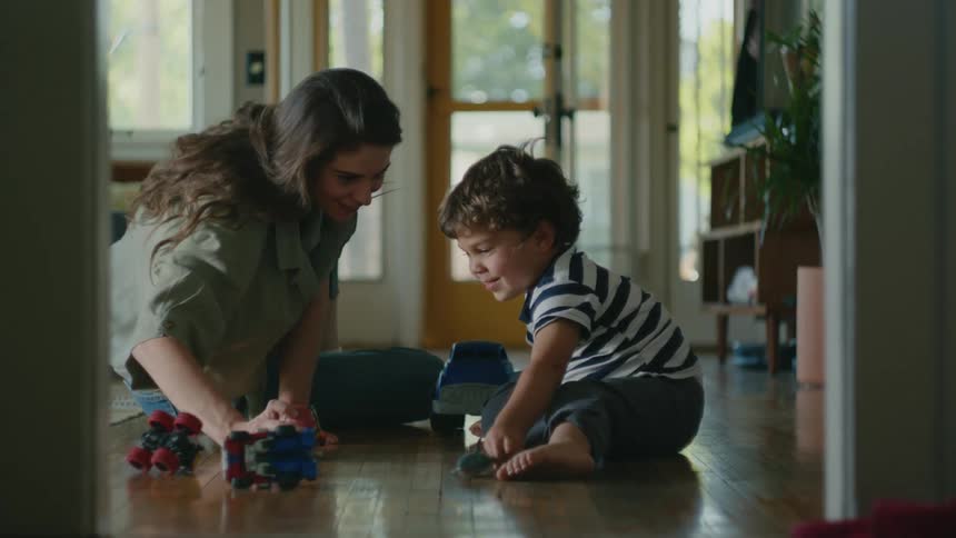 A boy and his mom play with a toy shark while sitting on the floor in their house