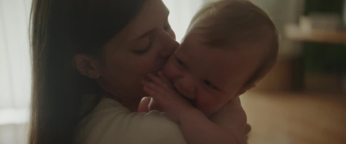 A woman kisses a baby on the cheek before the baby begins to play with her face