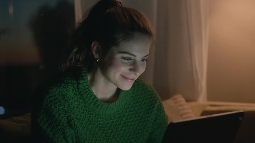 A woman laughs during a video call on her laptop at home