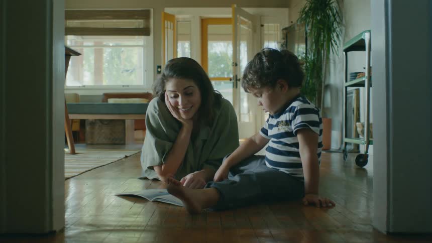 A woman reads to her son while sitting on the floor in their living room