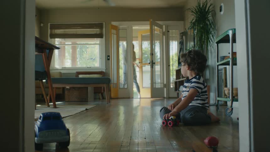 Child playing with toy cars watches mother walk out the front door