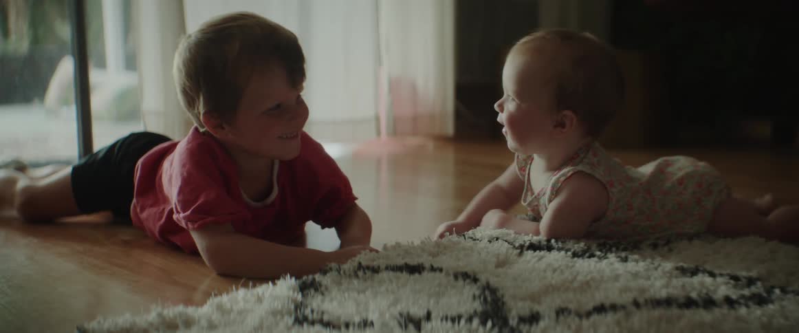 A young boy plays with a baby as they lay on the floor together