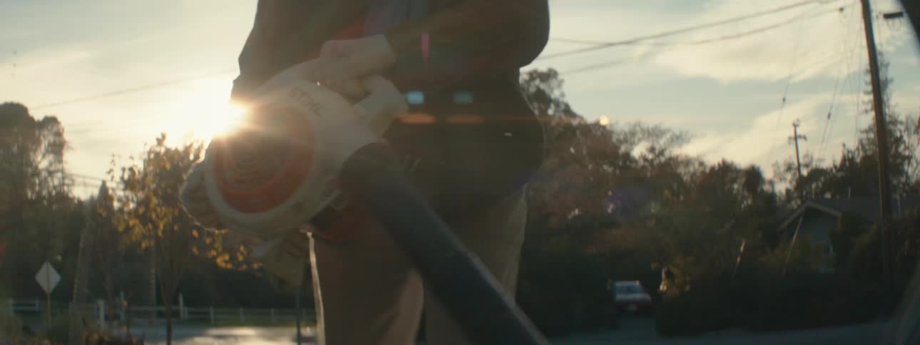 A man picks up a leaf blower and starts cleaning his front lawn