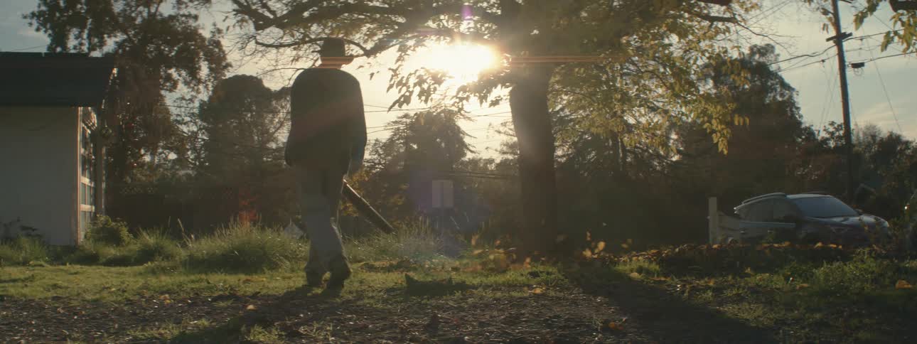 A man uses a leaf blower to leaves through a yard