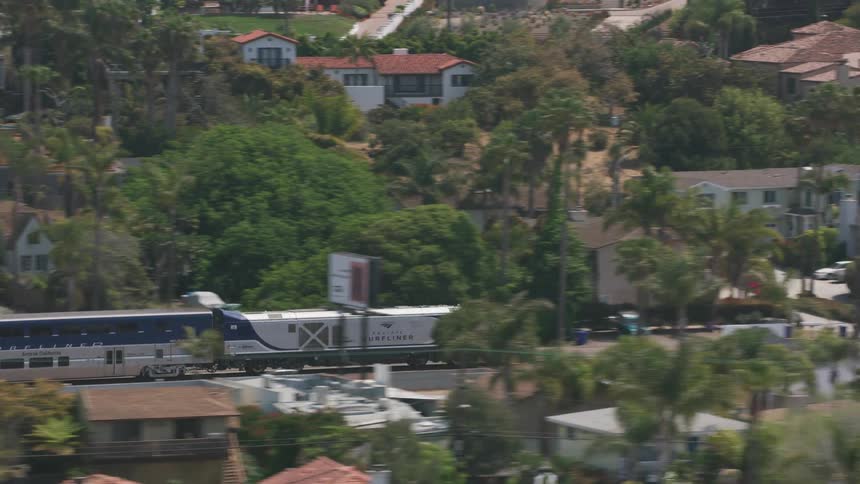 A train travels along a railway through a residential area during the day