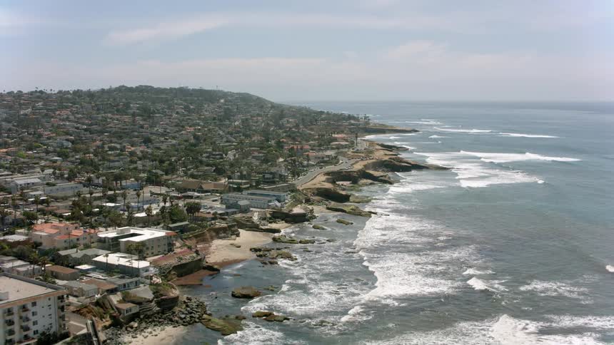Waves roll into shore as traffic moves on a road near a coastal community