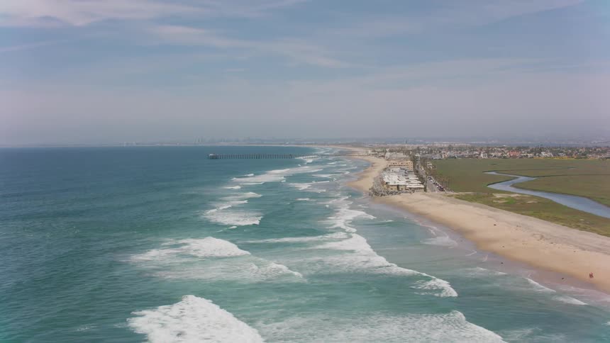 An aerial view of waves rolling in to the shore with hotels on the beach and houses in the distance