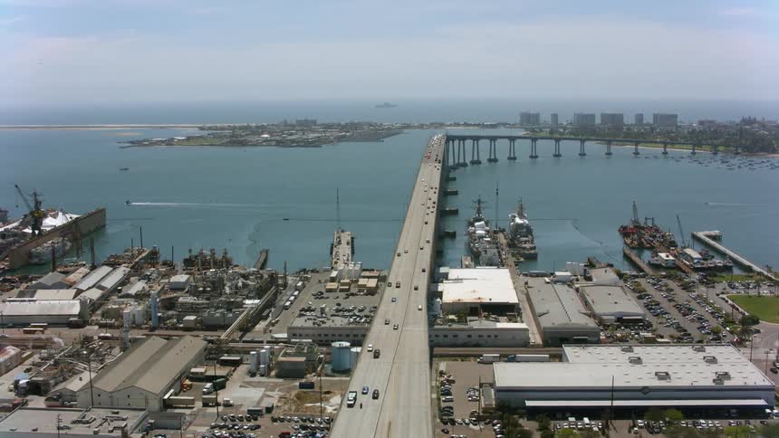 Traffic moves across a bridge on the coast passing ships in the harbor and traveling over the water