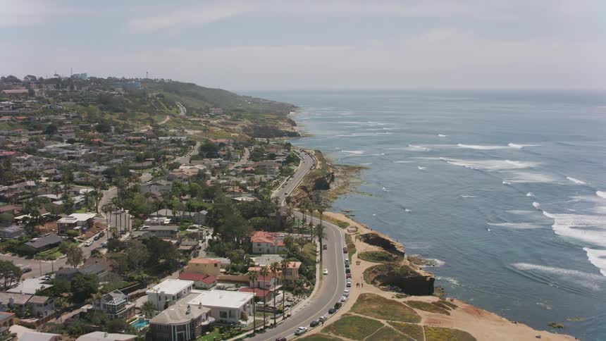 Waves roll into shore as traffic moves on a road near a coastal community