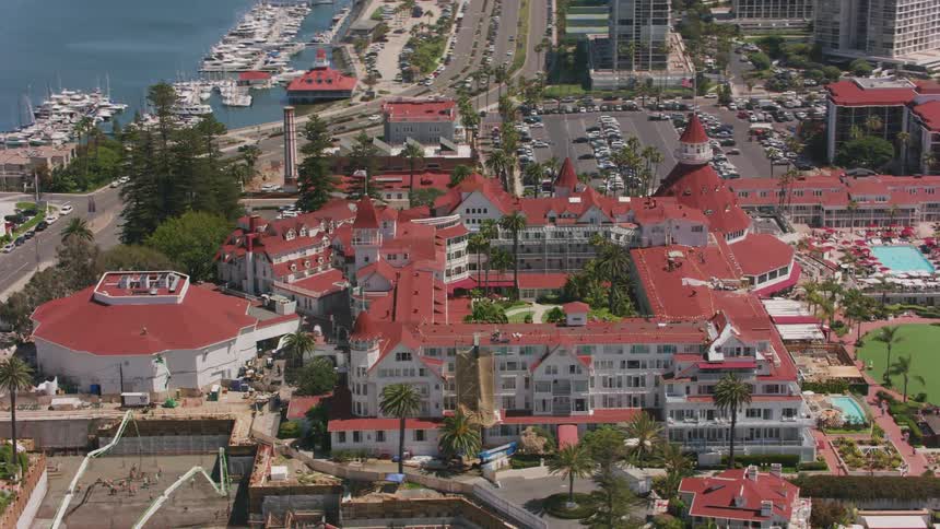 An aerial view of a hotel on the shore with cars driving down a street and boats in the water