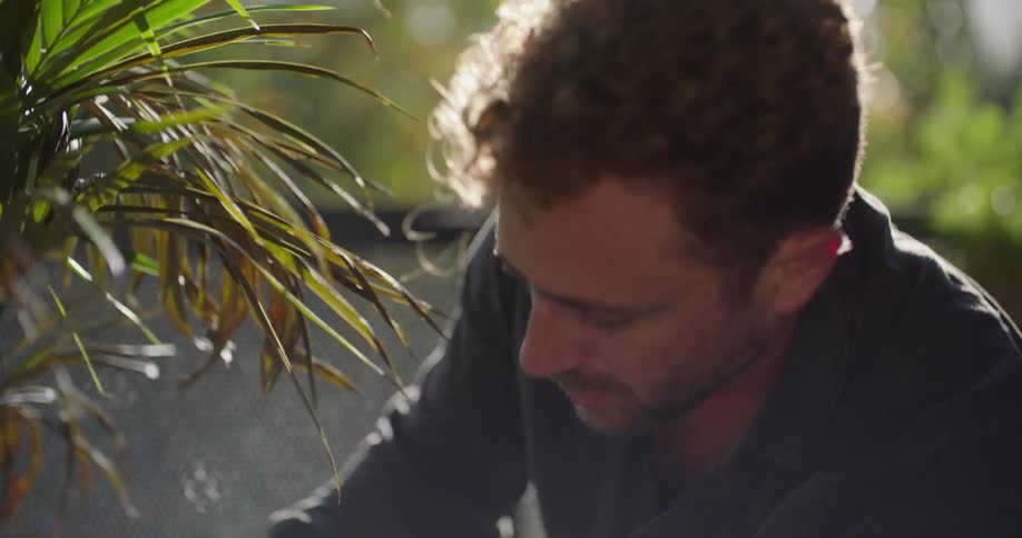 A man is sitting outside putting soil around a plant in a pot