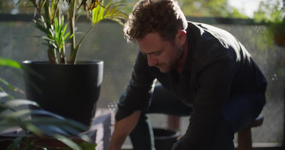 A man sits at home and scoops dirt in a planter