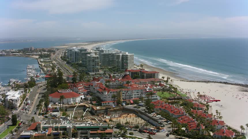 Aerial view of hotel del coronado and cars are on the street and in the parking lot as waves roll over the beach along the coast