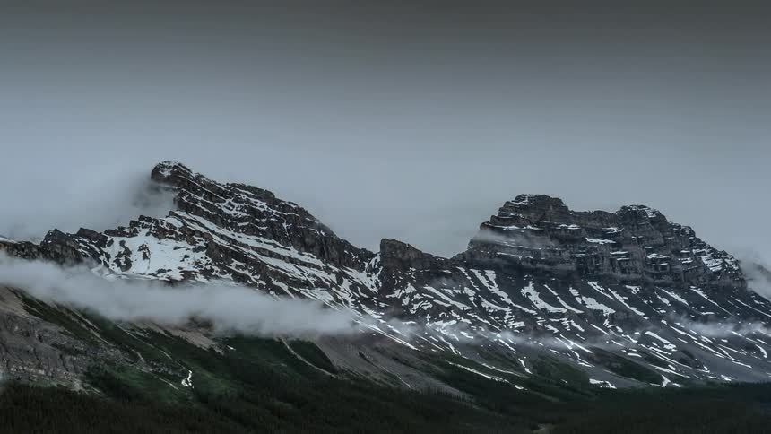 Clouds form around snowy mountains