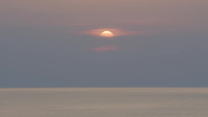Sun setting behind the clouds over the calm surface of the ocean