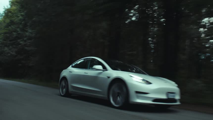 A car travels along a road through a forest during the day
