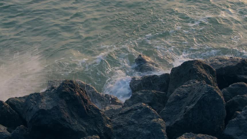 Ocean waves wash into a pile of rocks on the shore during the day