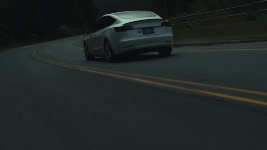 A car travels along a road through a forest at the base of a mountain during the day