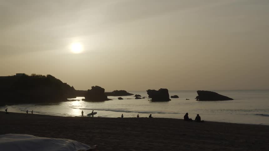 Sun shines from overcast sky onto beach goers and surfers
