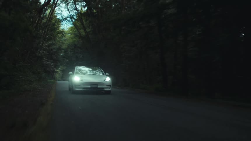 A car traveling on a narrow tree lined road with headlights on