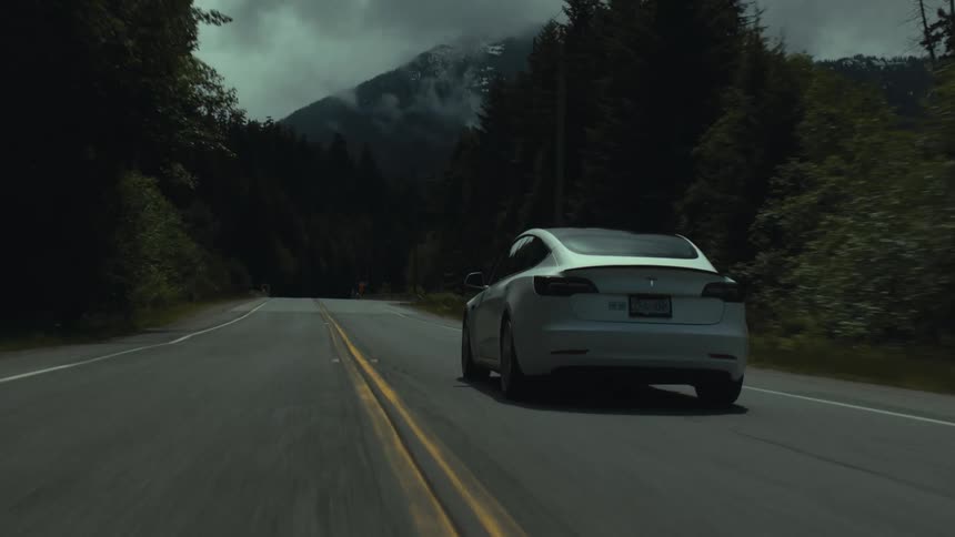 Car drives along highway toward misty mountain and past conifer forest