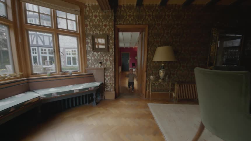 A young boy happily runs down a hallway and through a house towards a window