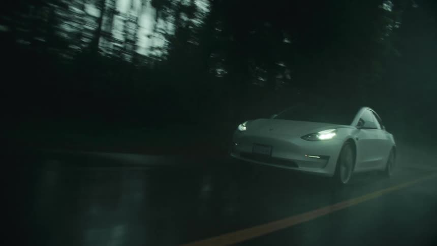 A car travels along a wet road through a woodland on a cloudy day