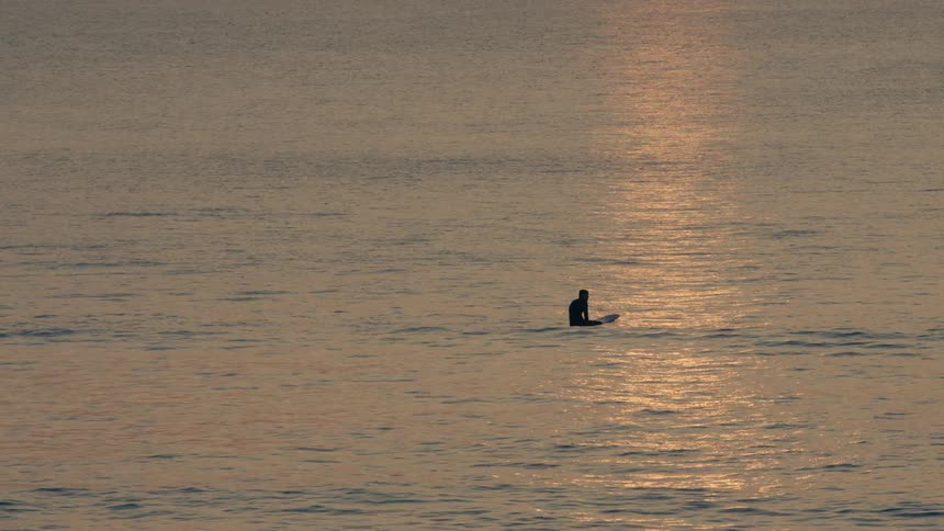 A person is floating on their surfboard in the ocean