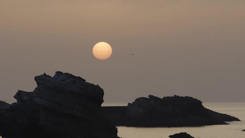 The moon looming over rock formations on the ocean at sunset