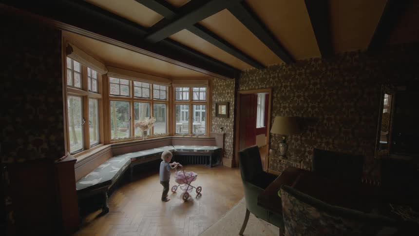 Toddler pushes a pink stroller through the living room of a house